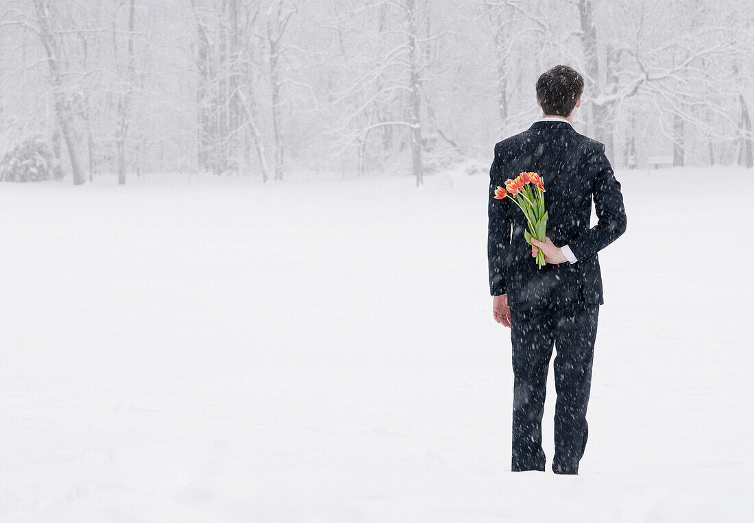 Geschäftsmann im Schneesturm versteckt Tulpenstrauss hinter seinem Rücken, Englischer Garten, München, Bayern, Deutschland