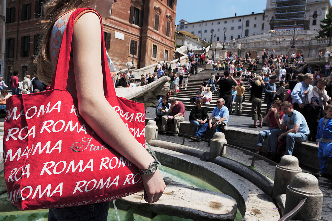 Junge Frau mit einer roten Romtasche am Fontana della Barcaccia auf der Piazza di Spagna, Spanische Treppe im Hintergrund, Rom, Italien
