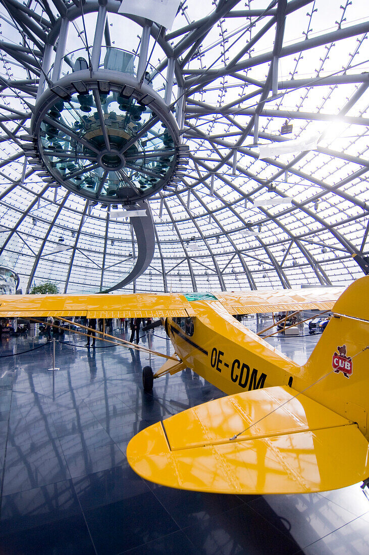Gelbes Flugzeug unter moderner Glaskuppel bei Gegenlicht im Museum Hangar 7, Salzburg, Österreich