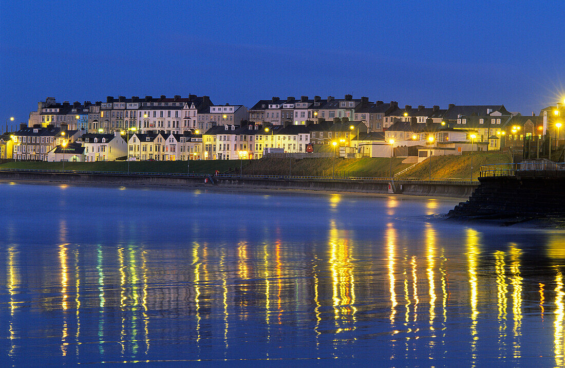 Blick auf beleuchtete Häuser an der Küste am Abend, Portrush, County Antrim, Irland, Europa