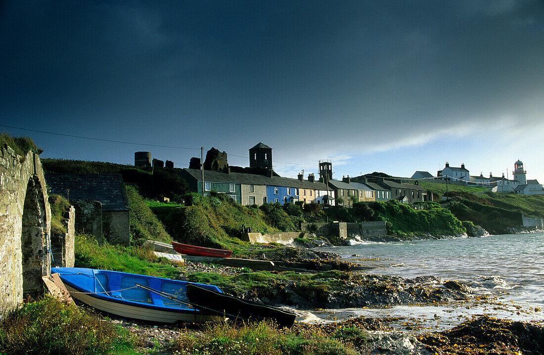 Houses and lighthouse on shore under thunder clouds, Roche's Point, County Cork, Ireland, Europe
