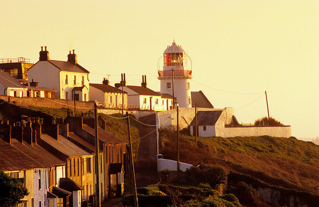 Häuser und Leuchtturm an der Küste im Licht der Abendsonne, Roche's Point, County Cork, Irland, Europa