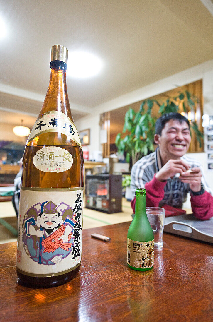 Blick auf Sakeflasche und grinsenden Mann in einem Lokal, Hokkaido, Japan, Asien