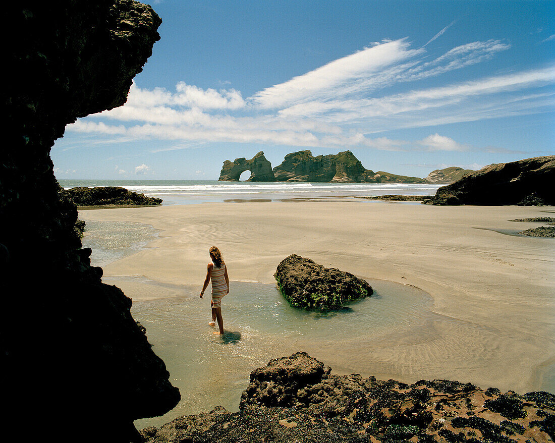 Frau läuft durch Tidenpools bei Ebbe am Wharariki Beach, Nordwestküste, Südinsel, Neuseeland