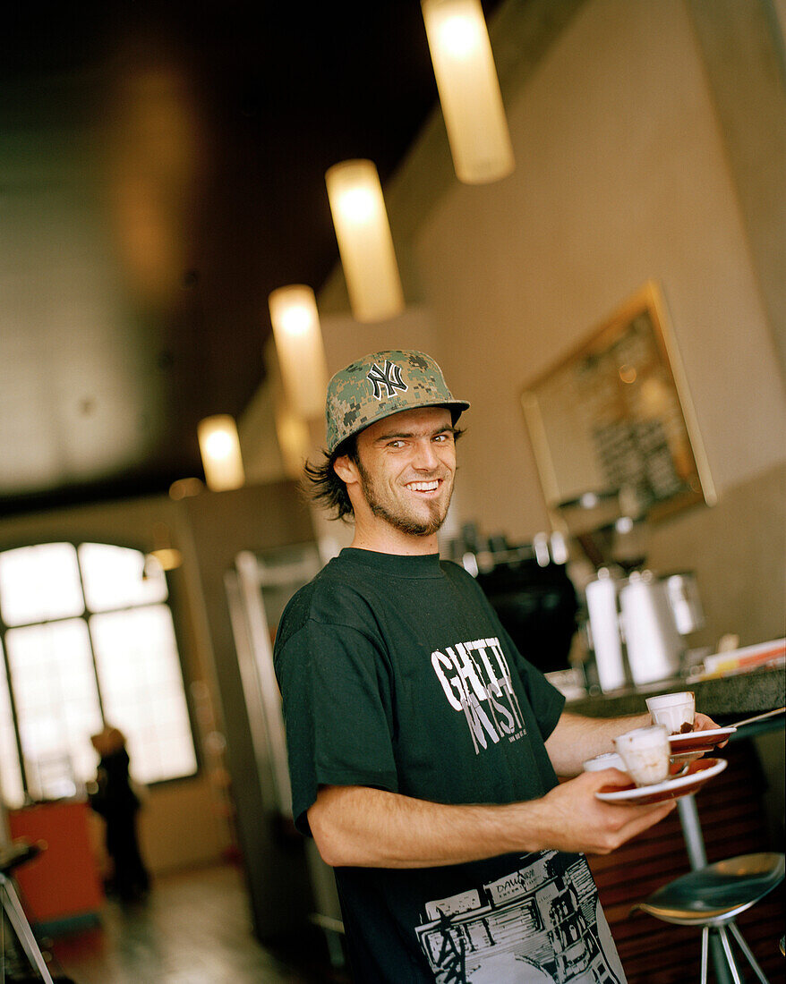 Smiling young man carrying trays at a chocolaterie and espresso bar, Tory Street, Wellington, North Island, New Zealand