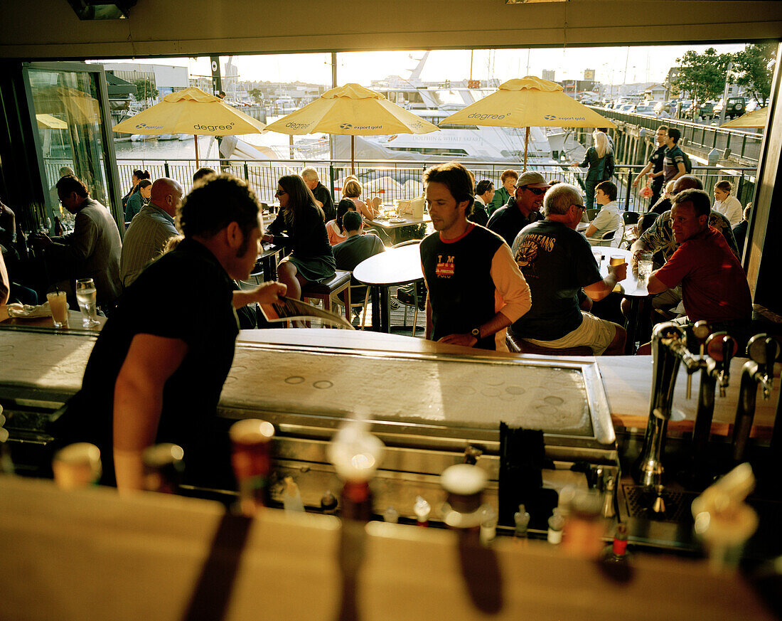 View fron the counter at people inside the Bar for yachtsmen in the evening, Viaduct Harbour, Auckland, North Island, New Zealand