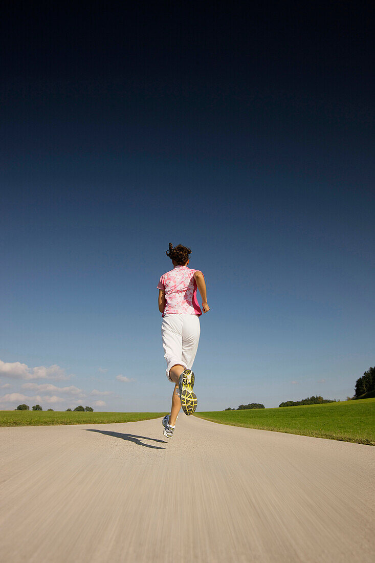 Frau joggt über Landstraße, Münsing, Bayern, Deutschland
