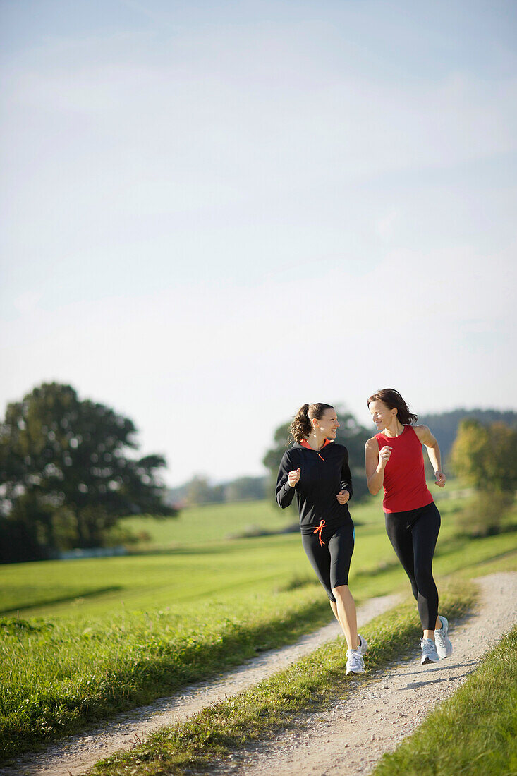Two women running along dirt road, Munsing, Bavaria, Germany