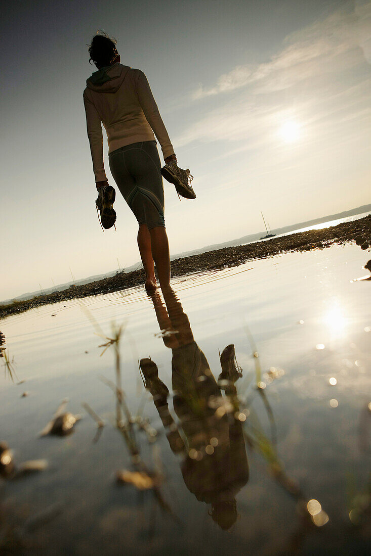 Barefoot female jogger standing at lake Starnberg, Ambach, Bavaria, Germany