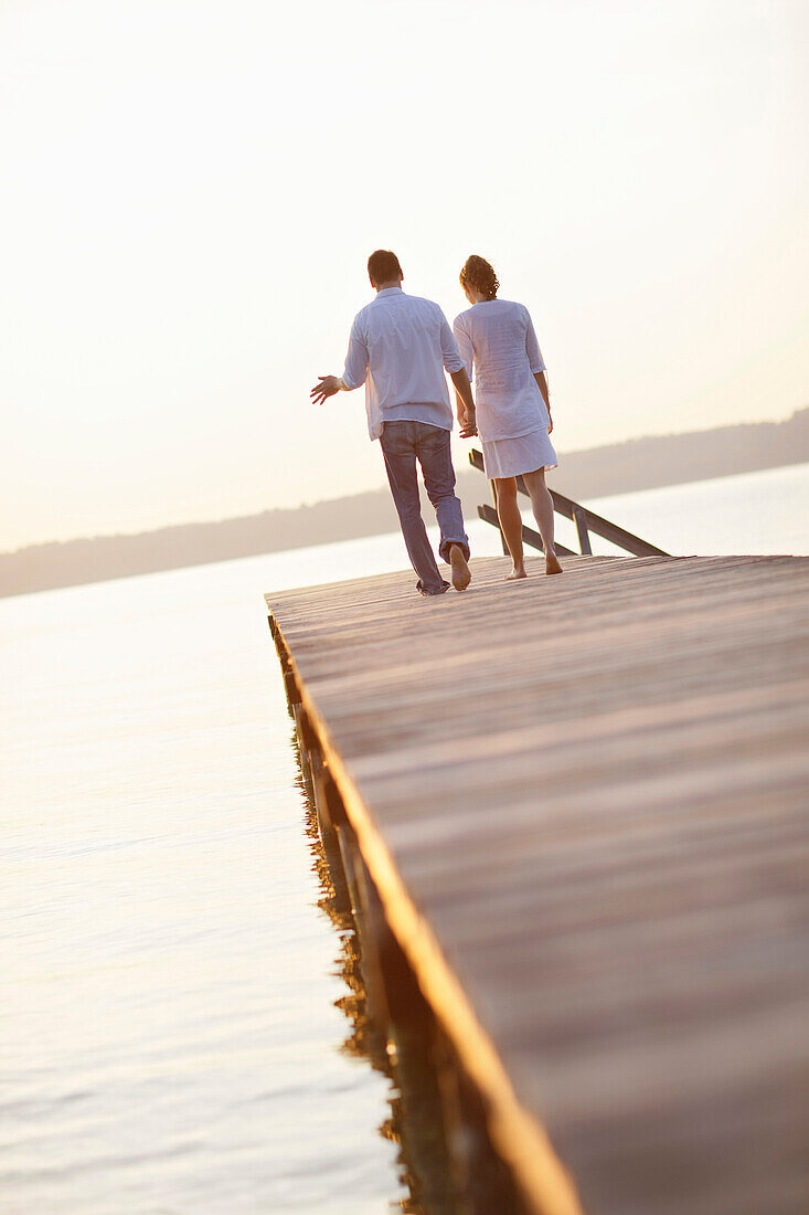 Couple walking over a jetty, Ambach, Lake Starnberg, Bavaria, Germany