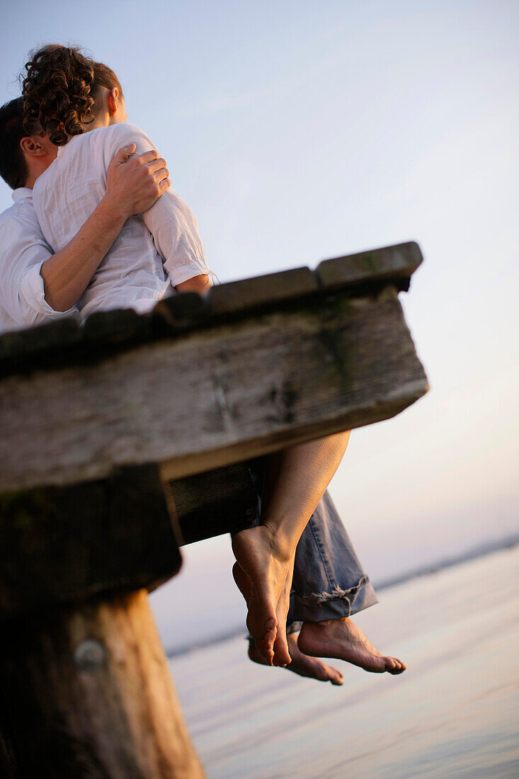 Couple sitting on a jetty, Ambach, Lake Starnberg, Bavaria, Germany