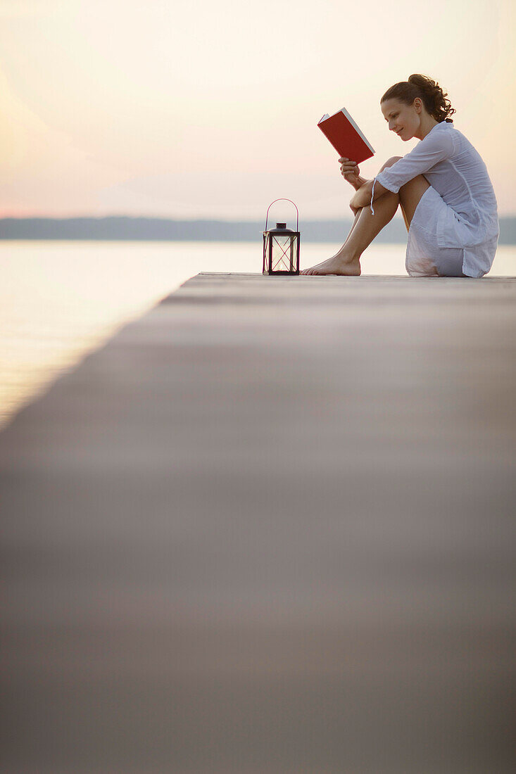 Woman sitting on jetty at lake Starnberg … – License image – 70215926 ...