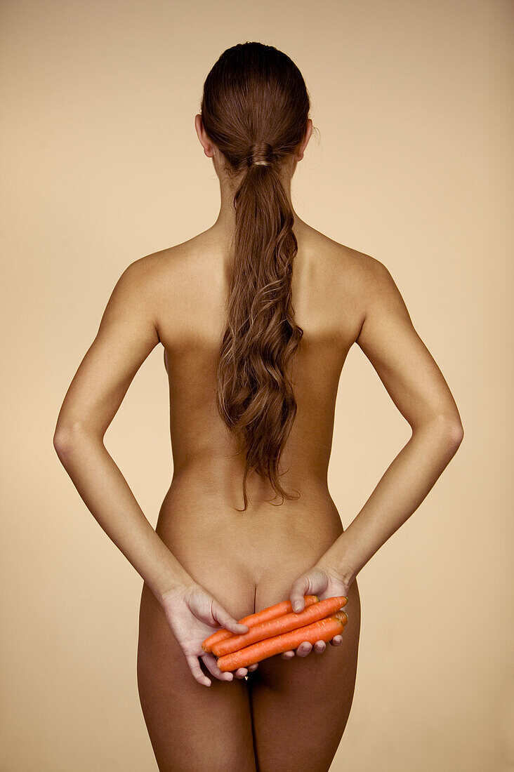 Nackte Frau mit Karotten hinter dem Rücken
