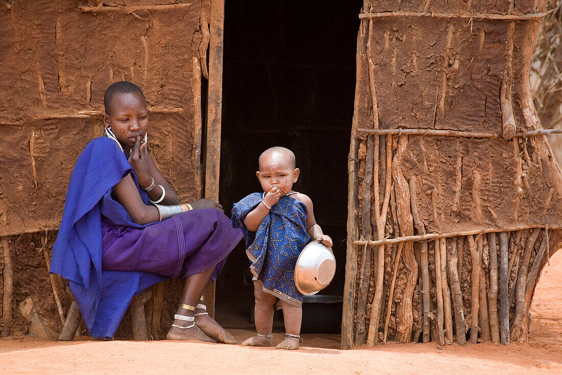 Massai Frau mit kleinem Kind sitzt vor einer Lehmhütte, Tsavo, Kenia, Afrika