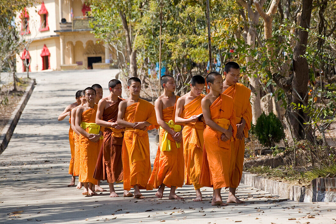 Buddhistic monks walking on a street in front of the monastery Vat Pa Phonphao, Luang Prabang, Laos