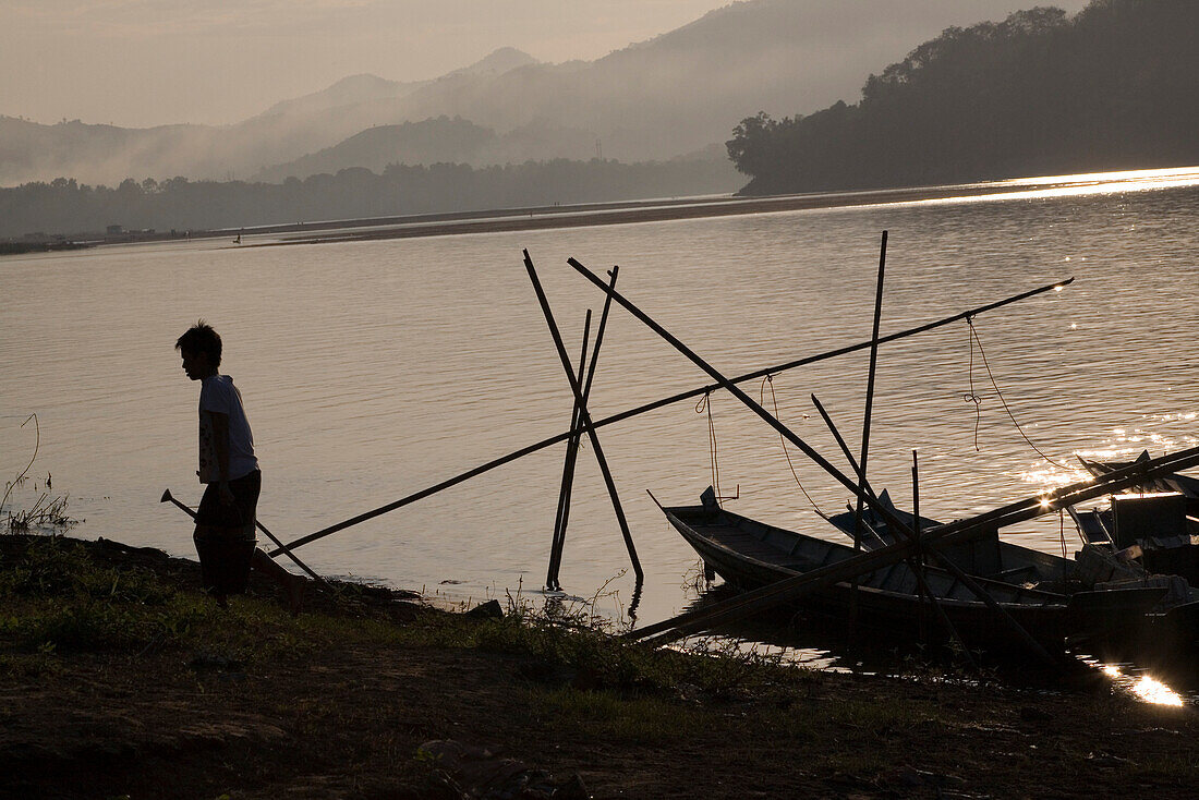 Silhouette eines Jungen mit Giesskanne am Ufer des Flusses Mekong, Luang Prabang, Laos