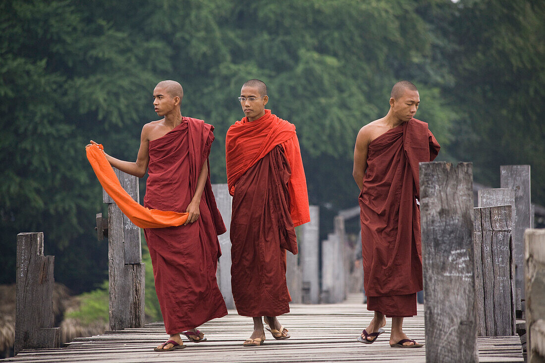 Three young buddhistic monks walking on the U Beins Bridgein Amarapura near Mandalay, Myanmar, Burma