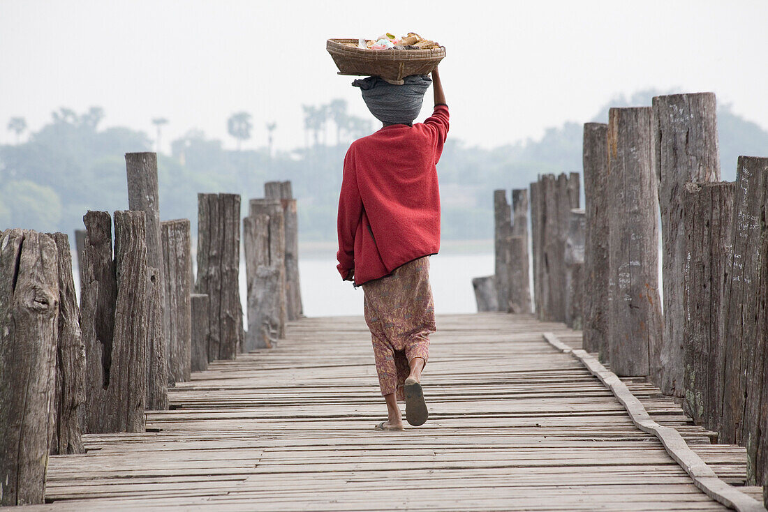 Burmese women, seen from behind carrying a basket on her head while  walking on the U Beins Bridge in Amarapura near Mandalay, Myanmar, Burma