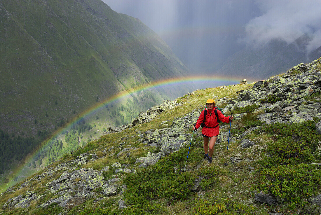 Frau beim Wandern im Regen mit Regenbogen über dem Pfossental, Texelgruppe, Ötztaler Alpen, Südtirol, Italien
