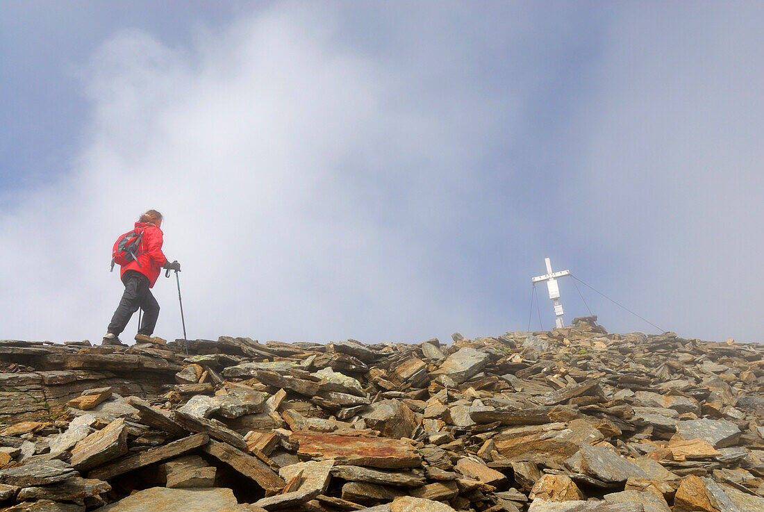 young woman reaching cross on summit glowing in the sun on Spielmann, Hohe Tauern range, National Park Hohe Tauern, Salzburg, Austria