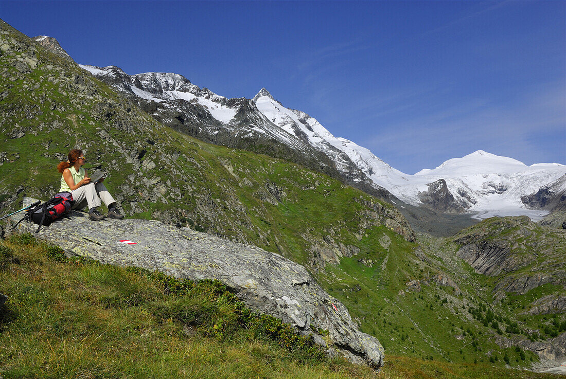 Frau rastet auf einem Felsen, Großglockner im Hintergrund, Nationalpark Hohe Tauern, Kärnten, Österreich