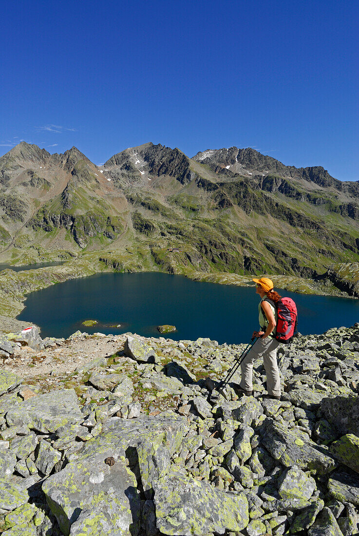 young woman hiking with view to lake Kreuzsee, Wangenitzsee, hut Wangenitzseehuette and Petzeck, Schobergruppe range, Hohe Tauern range, National Park Hohe Tauern, Carinthia, Austria