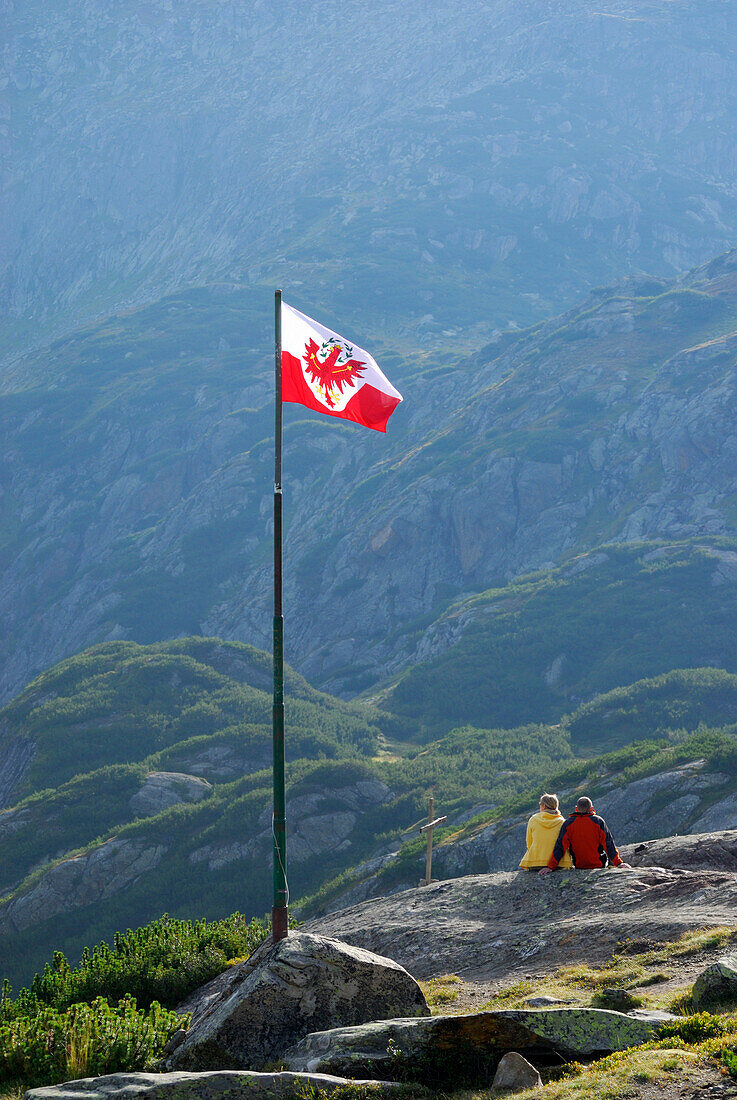 couple beneath Tyrolean flag, hut Sulzenauhuette, Stubaier Alpen range, Stubai, Tyrol, Austria