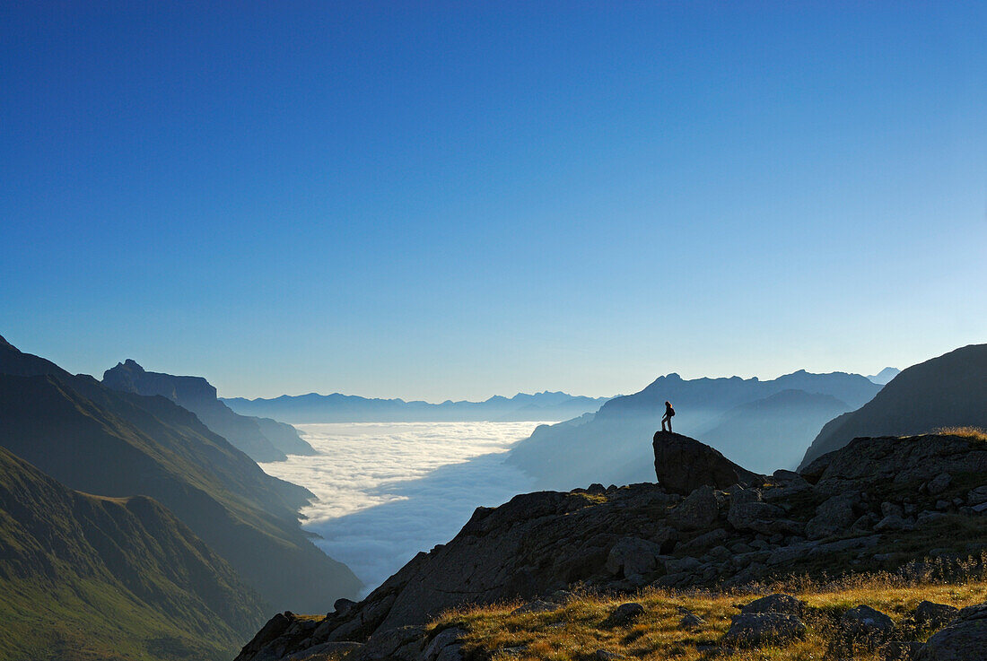 hiker on crag above fog bank in valley Gschnitztal, Kirchdachspitze in background, Bremer Huette, Stubaier Alpen range, Stubai, Tyrol, Austria