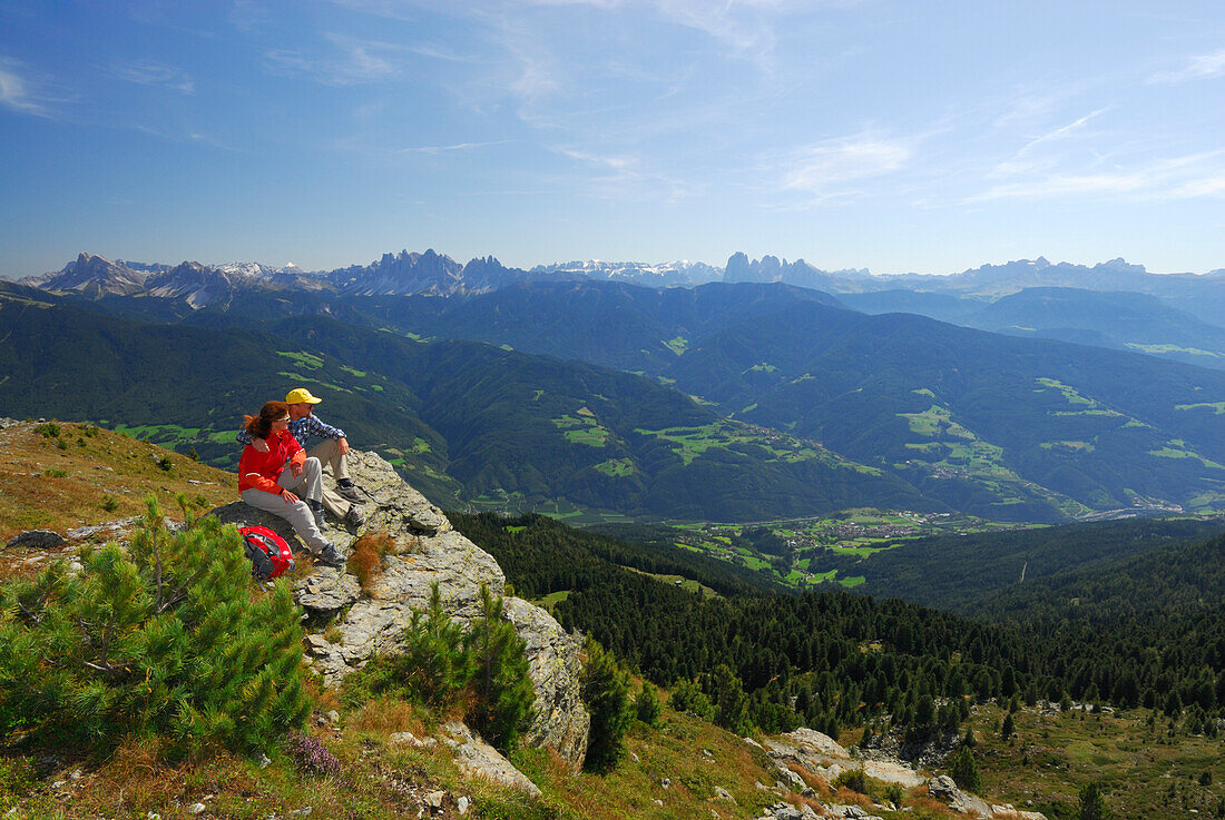 Paar auf Felsabsatz sitzend mit Blick auf Eisacktal und in die Dolomiten mit Peitlerkofel, Geislergruppe, Sella, Langkofelgruppe und Rosengarten, Radlseehütte, Sarntaler Alpen, Südtirol, Italien