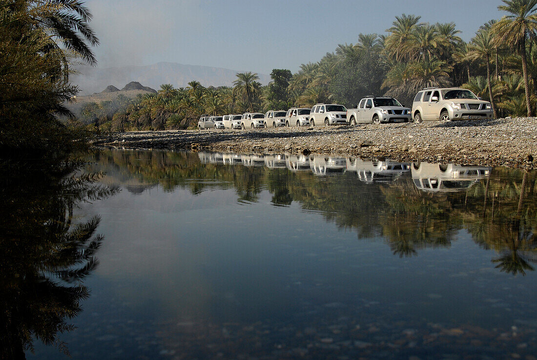 A row of all-terrain vehicles driving along a river, Al Hajar mountains, Wadi, Oman, Asia