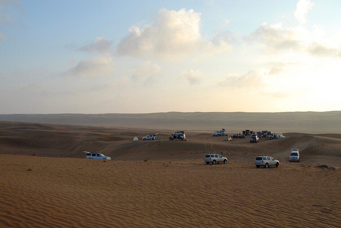 Geländewagen stehen bei Sonnenaufgang im Wüstensand, Wahiba Sands, Oman, Asien