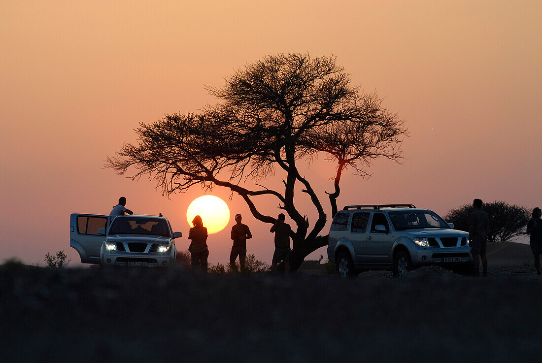 Menschen und Geländewagen vor der untergehenden Sonne, Al Hajar Berge, Oman, Asien