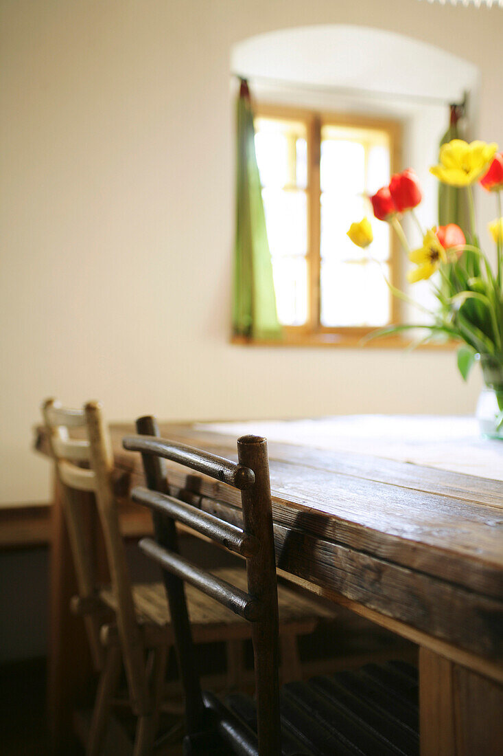 Zwei rustikale Holzstühle an einem Holztisch mit einem Strauss roter und gelber Tulpen