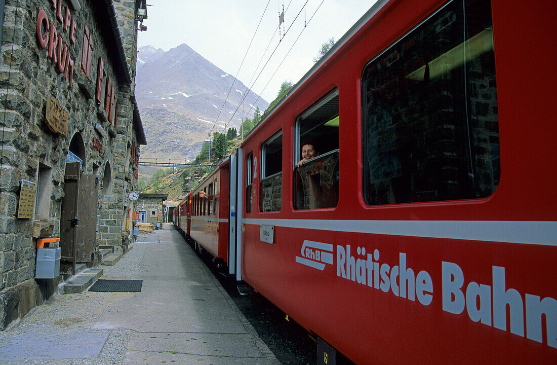 Frau lächelt aus dem Fenster eines roten Zugs der Rhätischen Bahn im Bahnhof der Alpe Grüm, Alp Grüm, Ferrovia Raetia, Bernina, Berninagruppe, Puschlav, Graubünden, Schweiz