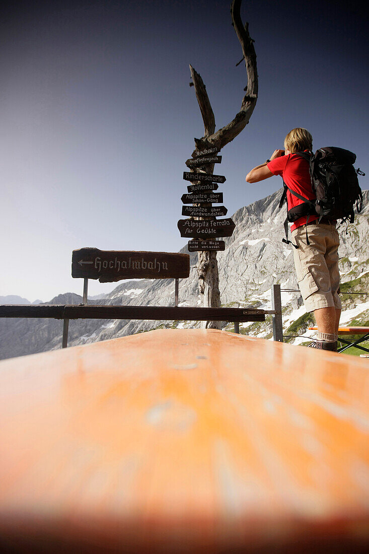 Junger Mann mit Fernglas auf einer Terasse einer Berghütte, Werdenfelser Land, Bayern, Deutschland