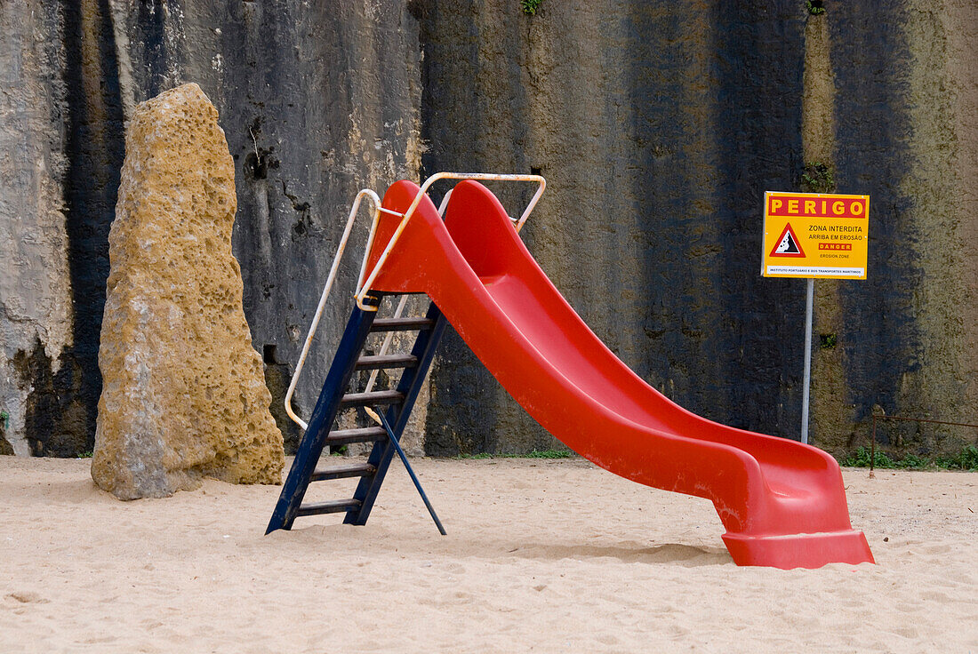 Red slide in a playground with danger sign, Ericeira, Portugal, Atlantic