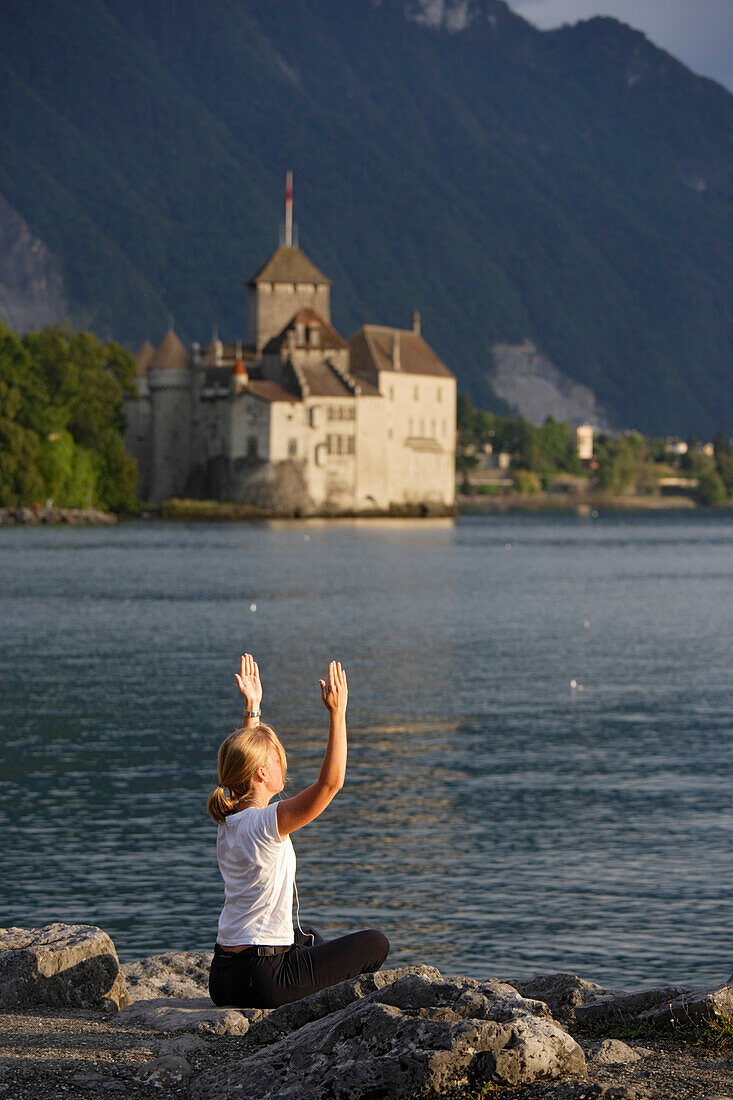Frau macht Yoga am Strand des Genfersee, Schloss Chillon im Hintergrund, Veytaux, Waadt, Schweiz