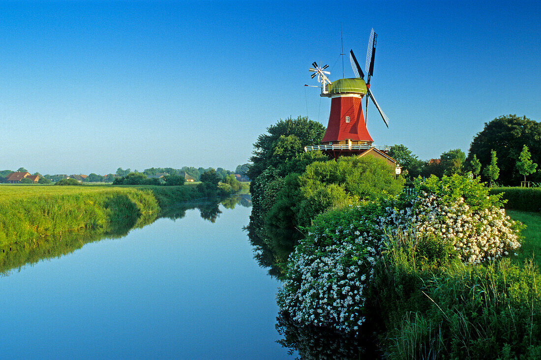Windmühle an einem Kanal unter blauem Himmel, Greetsiel, Ostfriesland, Niedersachsen, Deutschland