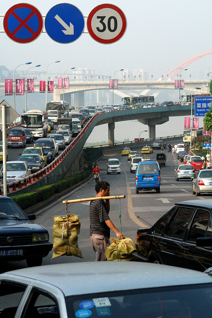 Mann trägt schwere Last durch die Rushhour der Straßen von Chongqing, China, Asien