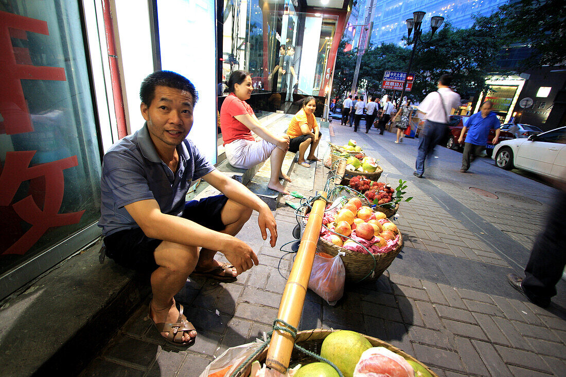 Lächelnder Straßenhändler sitzt vor seinem Obstkorb in Chongqing, China, Asien