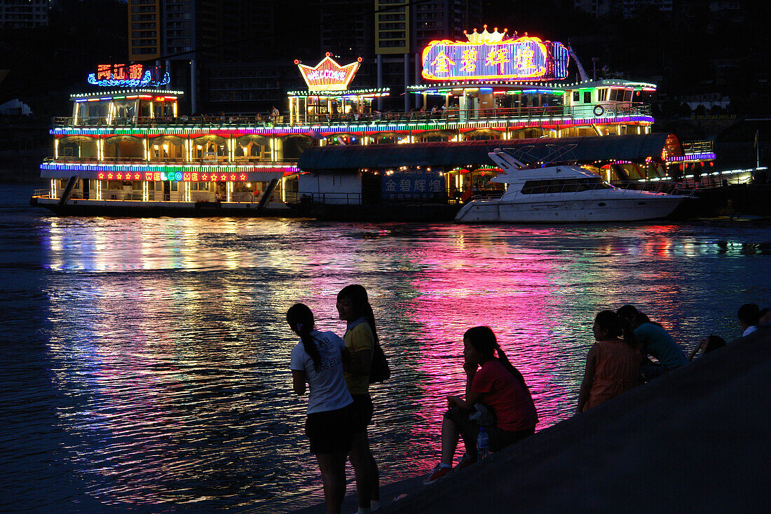 Eine Gruppe von Menschen geniessen die Lichter des schwimmenden Restaurants am Flußufer am Abend, Chongqing, China, Asien
