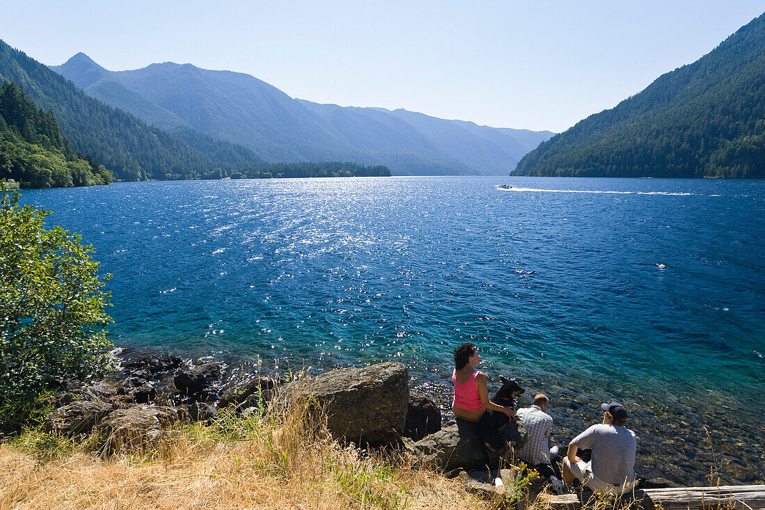 Menschen sitzen am Ufer des Lake Crescent im Sonnenlicht, Olympic Nationalpark, Washington, USA