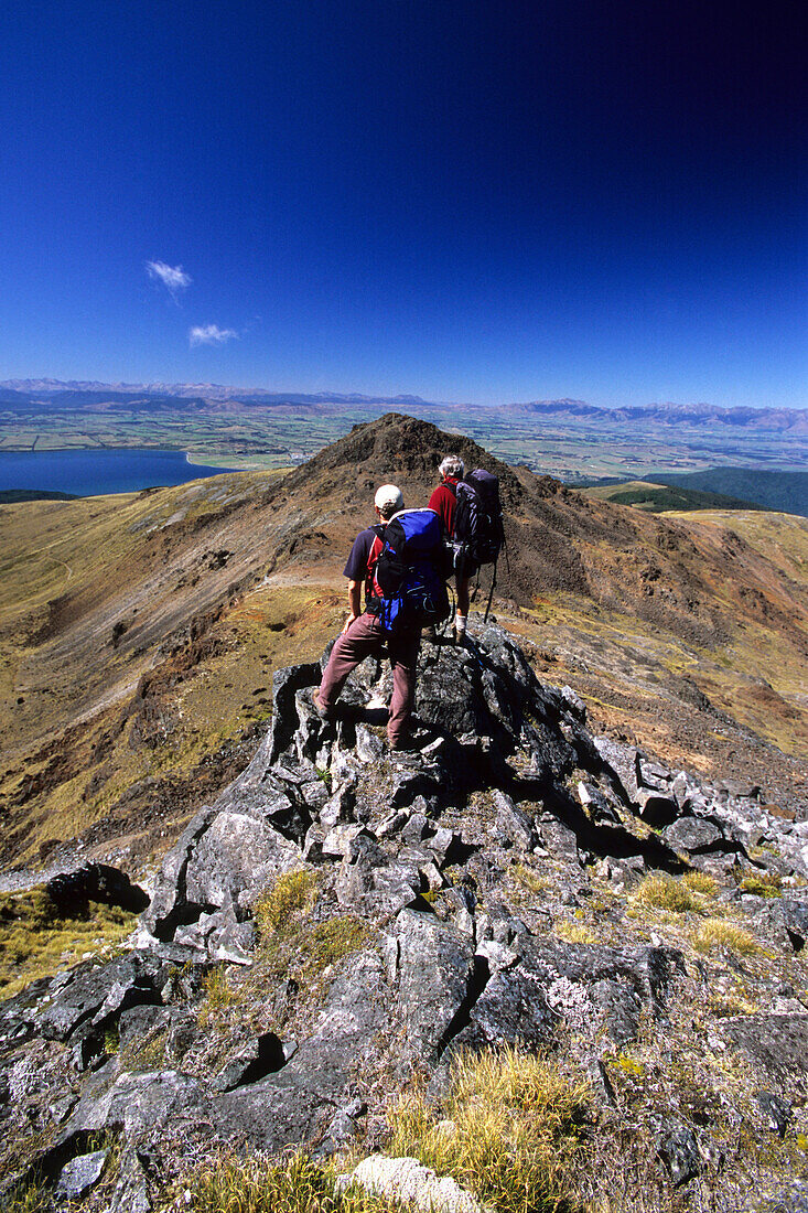 Two trekkers climbing onto Mount Luxmoore at the Kepler Mountains, view at Lake Te Anau, Fiordland National Park, South Island, New Zealand, Oceania