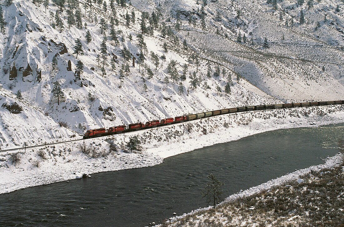 CP Rail train travels under snow covered cliffs in the Thompson River canyon. British Columbia, Canada