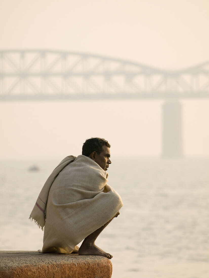 A pilgrim watches life along the holy river Ganges, an important pilgrimge site for Hindu's, in Varanasi, Uttar Pradesh, India