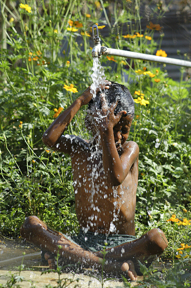 A boy having a shower under a water tap.