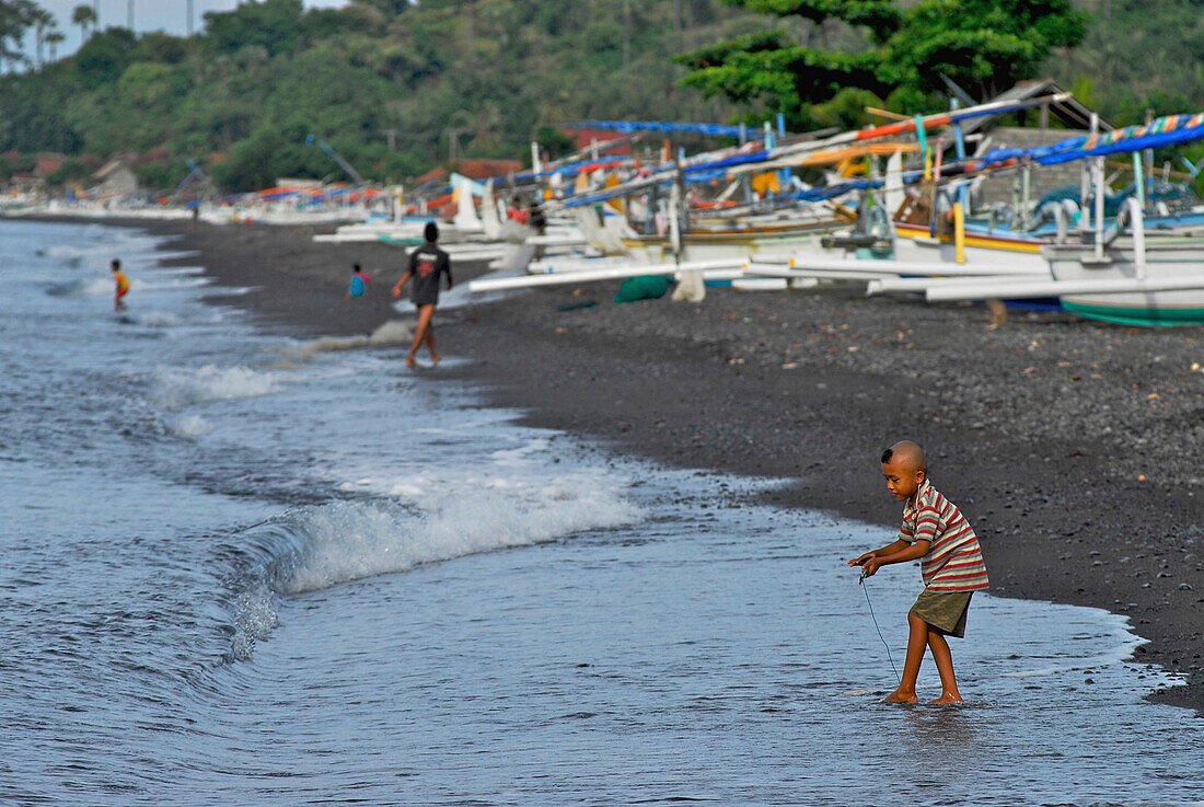 Fischerboote am Strand und spielendes Kind, Ost Bali, Indonesien, Asien