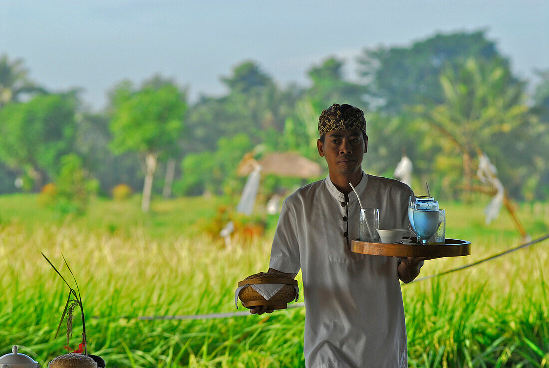 Balinesischer Kellner mit Tablett vor grüner Landschaft, Chedi Club, GHM Hotel, Ubud, Indonesien, Asien