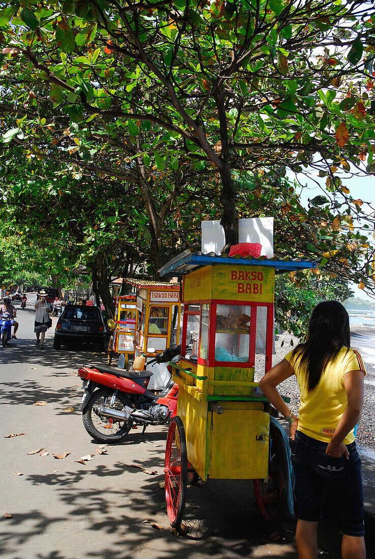 Eine Frau steht neben einem Imbisswagen am Strassenrand, Candi Dasa, Ost Bali, Indonesien, Asien