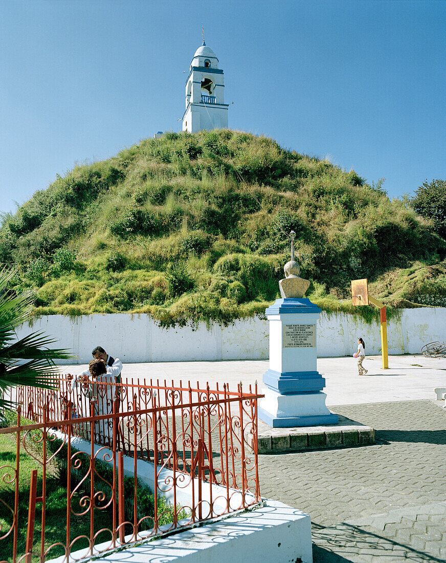 Glockenturm auf überwachsener Aztekenpyramide unter blauem Himmel, Dorf San Juan Xiutetelco, Provinz Puebla, Mexiko, Amerika